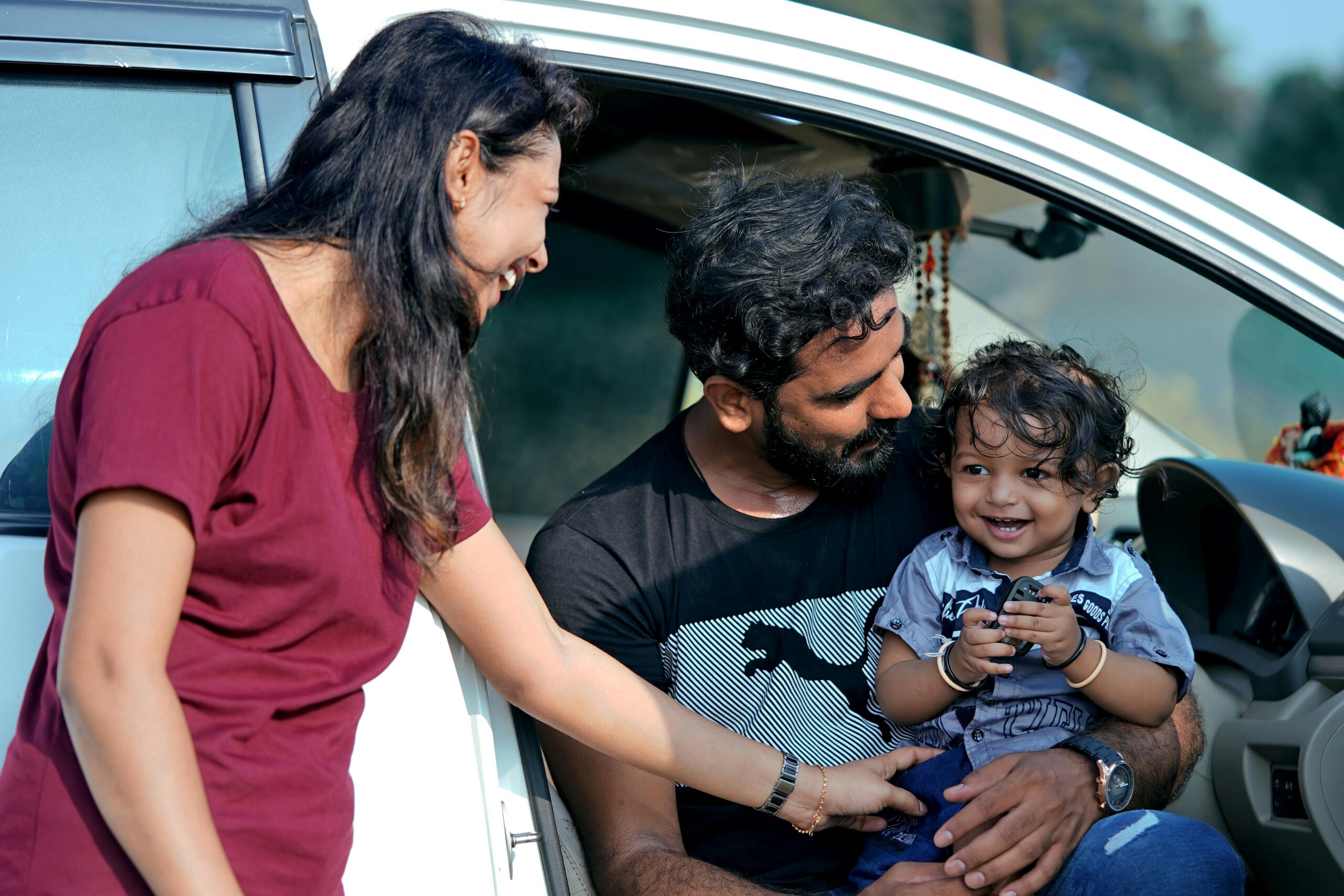 A joyful family moment with parents and child sitting in a car in Sanand, India.
