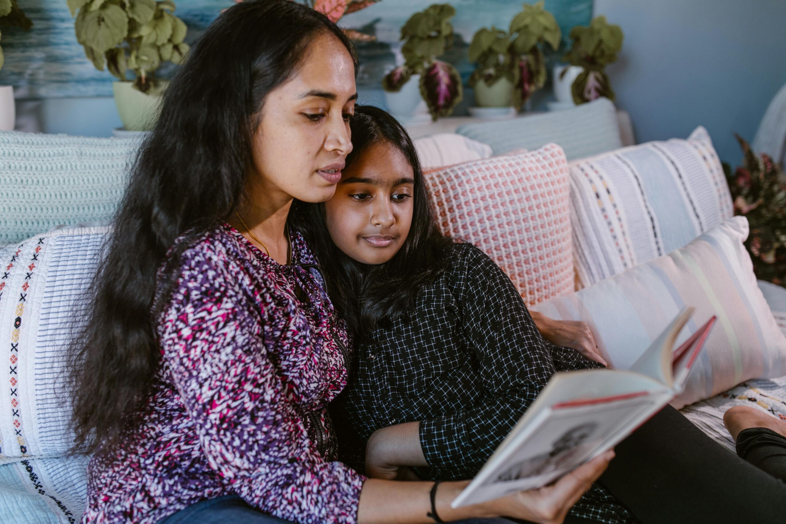 A mother and daughter sharing a book and quality time on a comfortable sofa indoors.